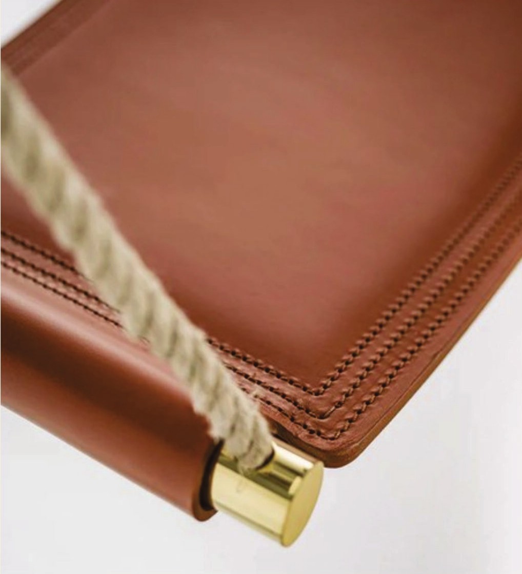 Indoor leather swing — tan saddle leather, white stitching, brass hardware.